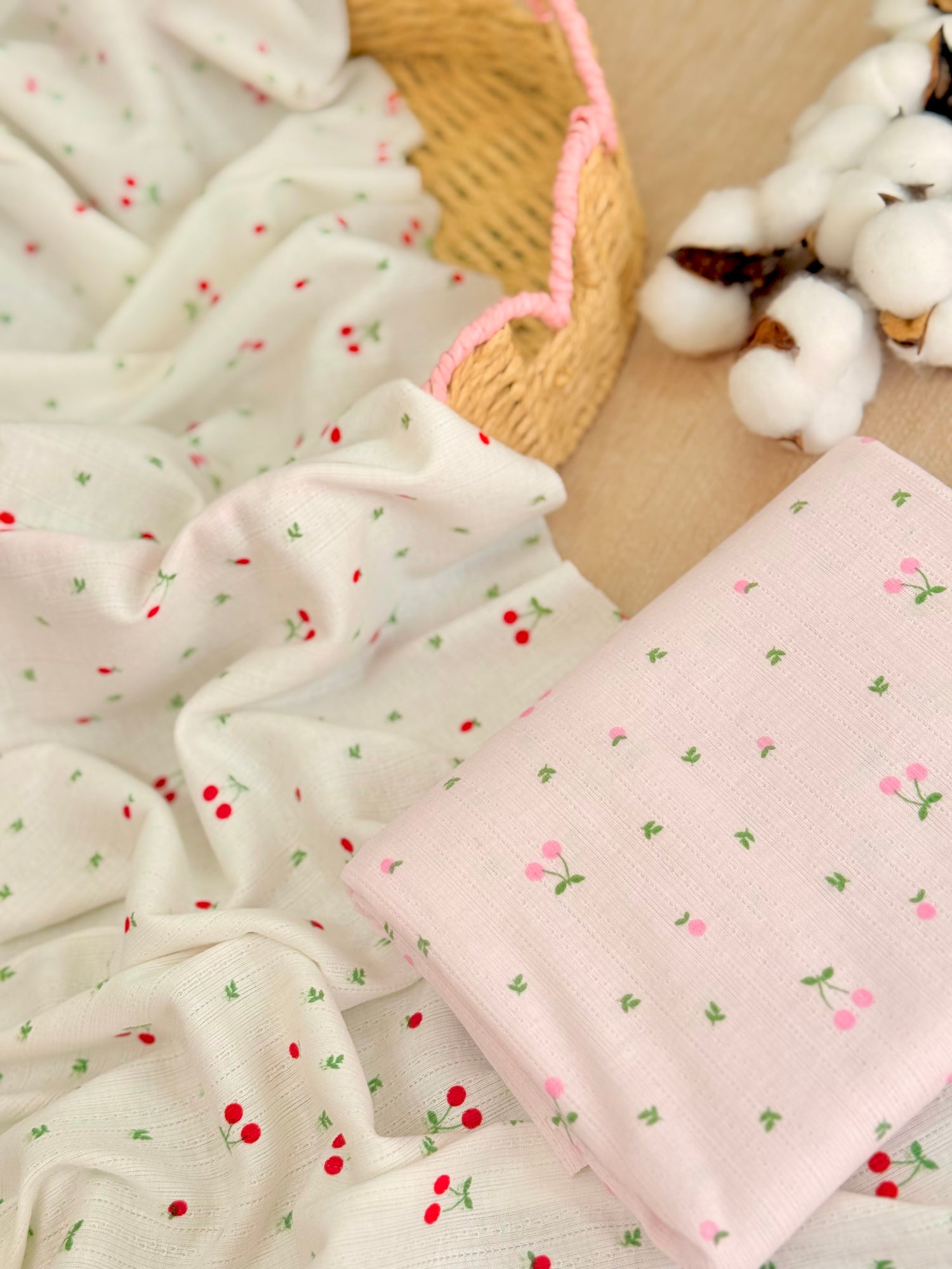 Tela jersey de algodón estampada Cherry Blossom con pequeñas cerezas sobre fondo blanco y rosa, ideal para playeras, vestidos, pijamas y ropa infantil.