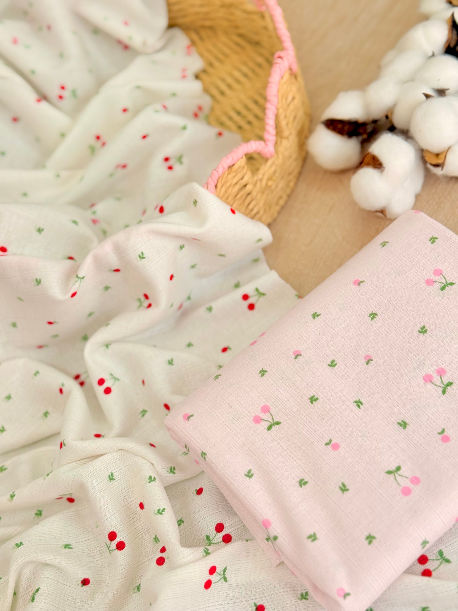 Tela jersey de algodón estampada Cherry Blossom con pequeñas cerezas sobre fondo blanco y rosa, ideal para playeras, vestidos, pijamas y ropa infantil.