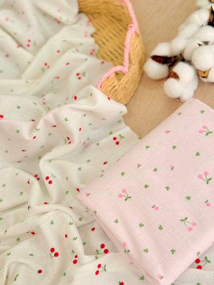 Tela jersey de algodón estampada Cherry Blossom con pequeñas cerezas sobre fondo blanco y rosa, ideal para playeras, vestidos, pijamas y ropa infantil.